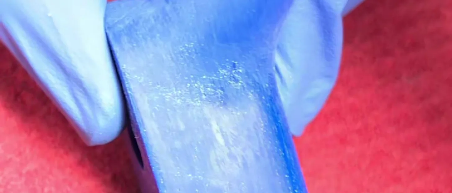 A blue printed part held in gloved fingers after the files. The layer lines are gone and the surface is left with a pale haze.